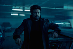 Butcher (Karl Urban) stands leaning against a car door